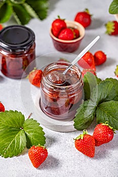 Fresh homemade strawberry jam in glass jar on a light background