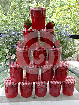 Fresh homemade strawberry jam in jars with garden background.