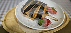 Fresh homemade striped chocolate croissant with chocolate filling on a round white plate, served with fresh strawberry