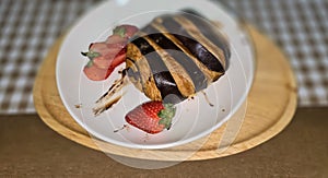 Fresh homemade striped chocolate croissant with chocolate filling on a round white plate, served with fresh strawberry