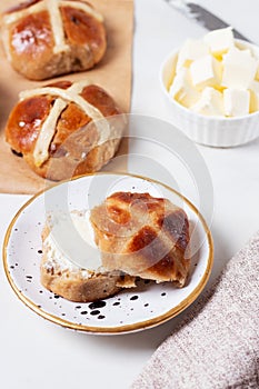 Fresh homemade Traditional Easter treats hot Cross Buns with raisins, served with butter and knife on marble bench top