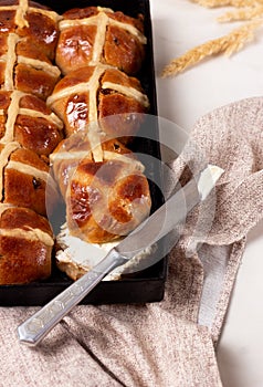 Fresh homemade Traditional Easter treats hot Cross Buns with raisins, served with butter and knife on marble bench top