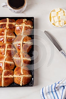 Fresh homemade Traditional Easter treats hot Cross Buns with raisins, served with butter and knife on marble bench top