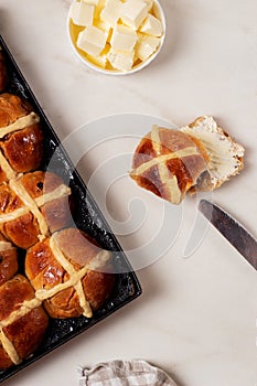 Fresh homemade Traditional Easter treats hot Cross Buns with raisins, served with butter and knife on marble bench top