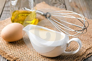 Fresh homemade white sauce Mayonnaise and ingredients eggs, lemon olive oil on wooden background