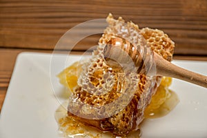Fresh honeycombs and wooden dipper with pouring honey on a wooden table