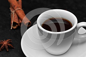 Fresh hot black coffee in white cup, coffee beans, cinnamon sticks, anise star on black background. Coffee time concept