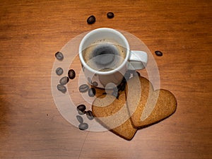 Fresh and hot espresso in white cup with coffee beans and heart shaped ginger bread around