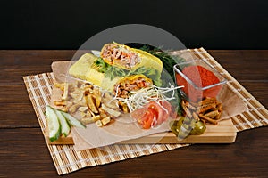 Fresh hot fragrant shawarma cut lies on a wooden board with vegetables, green leaves and fries