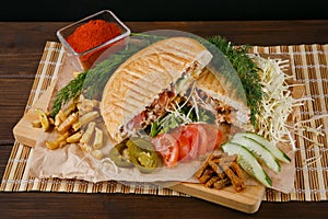 Fresh hot fragrant shawarma cut lies on a wooden board with vegetables, green leaves and fries