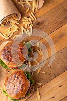 Fresh hot juicy burger with salty french fries. Meal on a cutting kitchen board on a wooden table. Tasty cheeseburger with cheese