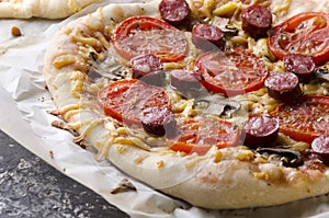 Fresh and hot, just cooked pizza with slices of sausage, tomatoes, mushrooms and melted cheese.Closeup of delicious traditional pi