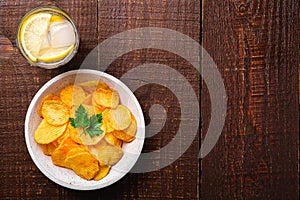 Fresh ice cold water drink with lemon near to fried potato chips with parsley leaf in wooden bowl on wood backdrop