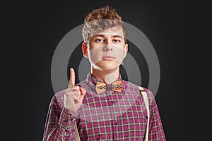 Fresh idea! Attention! Handsome young man in vintage shirt and curly hair keeping finger raised and looking at camera