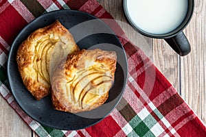 Fresh individual apple tarts on a black plate, cup of milk, red, green, and white cloth napkin, wood background