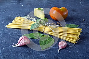 Fresh ingredients for cocking pasta with Traditiona Italian sauce Pesto. Dry Spaghetti, Basil leaves, tomato, parmesan on dark