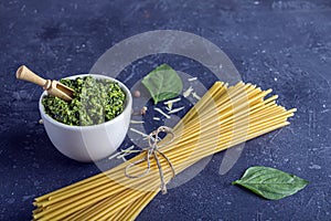 Fresh ingredients for cocking Traditiona Italian pasta. Cooked sauce Pesto, Dry Spaghetti and Basil leaves on dark background.