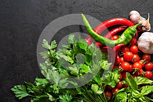 Fresh ingredients for cooking spicy sauce: cherry tomatoes, parsley, basil, garlic and chilli pepper on black background