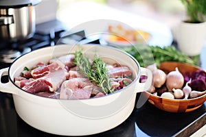fresh ingredients for coq au vin beside pot: thyme, bacon, mushrooms