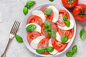 Fresh italian caprese salad with sliced tomatoes, mozzarella cheese, basil, olive oil and fork in a plate