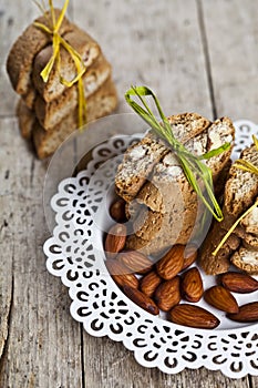 Fresh Italian cookies cantuccini stacked and almond seeds  on white plate closeup on ructic wooden table background