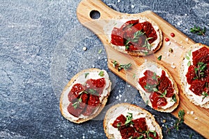 Fresh italian sandwiches with cream cheese and sun dried tomatoes on wooden kitchen board top view. Delicious snack and appetizer.
