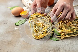 Fresh italian uncooked homemade pasta. Hands making pasta tagliatelle. Raw homemade spinach pasta