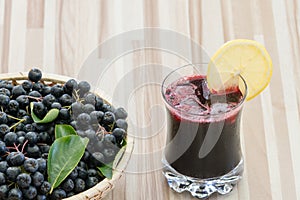 Fresh juice of chokeberry or Aronia melanocarpa in glass with ice and lemone slice, berry in basket