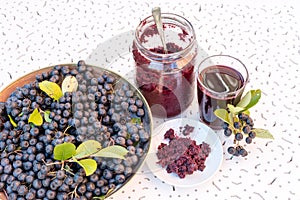 Fresh juice and jam of black chokeberry Aronia melanocarpa in glass and berry in pot on white textured background photo