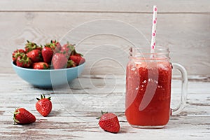 Fresh juice, shake, milkshake of strawberries in a mason jar with a straw. Pile of juicy ripe organic fresh strawberries in a