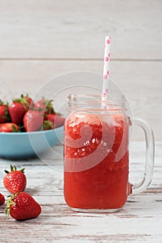 Fresh juice, shake, milkshake of strawberries in a mason jar with a straw. Pile of juicy ripe organic fresh strawberries in a