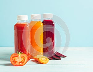 Fresh juice smoothies from a variety of vegetables carrots apple tomatoes beets in bottles on a wooden blue background.