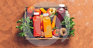 Fresh juice smoothies from a variety of vegetables carrots apple tomatoes beets bottles in wooden box brown background