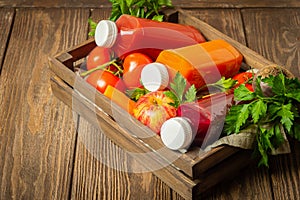 Fresh juice smoothies from a variety of vegetables carrots apple tomatoes beets bottles in wooden box brown background
