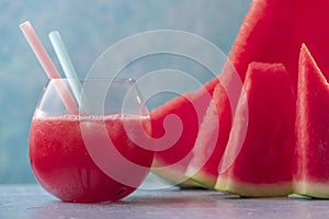 Fresh juice of sweet spanish watermelon in glass with straws and just cutted slices on blue background. Close up shot with