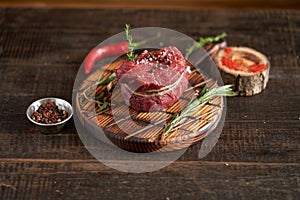 Fresh, juicy, aged fillet mignon steak tied with twine on a cutting board with spices - peas, dried tomatoes and paprika