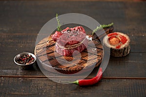 Fresh, juicy, aged fillet mignon steak tied with twine on a cutting board with spices - peas, dried tomatoes and paprika