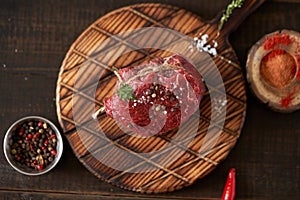 Fresh, juicy, aged fillet mignon steak tied with twine on a cutting board with spices - peas, dried tomatoes and paprika