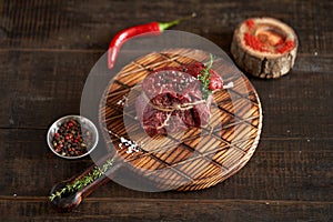 Fresh, juicy, aged fillet mignon steak tied with twine on a cutting board with spices - peas, dried tomatoes and paprika