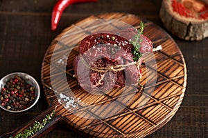 Fresh, juicy, aged fillet mignon steak tied with twine on a cutting board with spices - peas, dried tomatoes and paprika