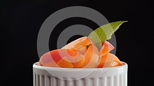 Fresh juicy apricot slices in a cup - rotate on black background
