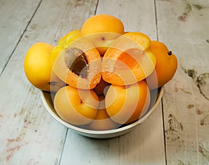 Fresh juicy apricots in a deep plate on a light wooden tabletop