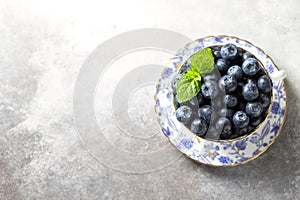 Fresh juicy blueberries in a vintage porcelain cup on a light concrete background. Healthy food or nutrition