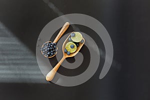 Fresh juicy blueberry fruits with limes on a wooden spoon against a dark background.