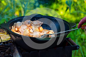 Fresh, juicy chicken legs are fried with onions in a cast-iron cauldron in vegetable oil. The chicken is thwarted with a scoop.