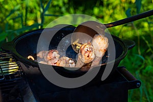 Fresh, juicy chicken legs are fried with onions in a cast-iron cauldron in vegetable oil. The chicken is thwarted with a scoop.