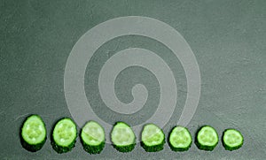 Fresh juicy chopped pieces of cucumber, evenly laid out in the form of a lower frame on a gray background