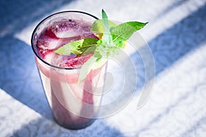 A fresh juicy glass with a fruit and berry drink, with a slice of lime, a sprig of mint and ice cubes