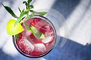 A fresh juicy glass with a fruit and berry drink, with a slice of lime, a sprig of mint and ice cubes