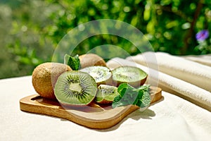 Fresh juicy kiwi and green mint leaves in plate on the table with linen tablecloth in the garden. Sliced ripe exotic fruits. Space
